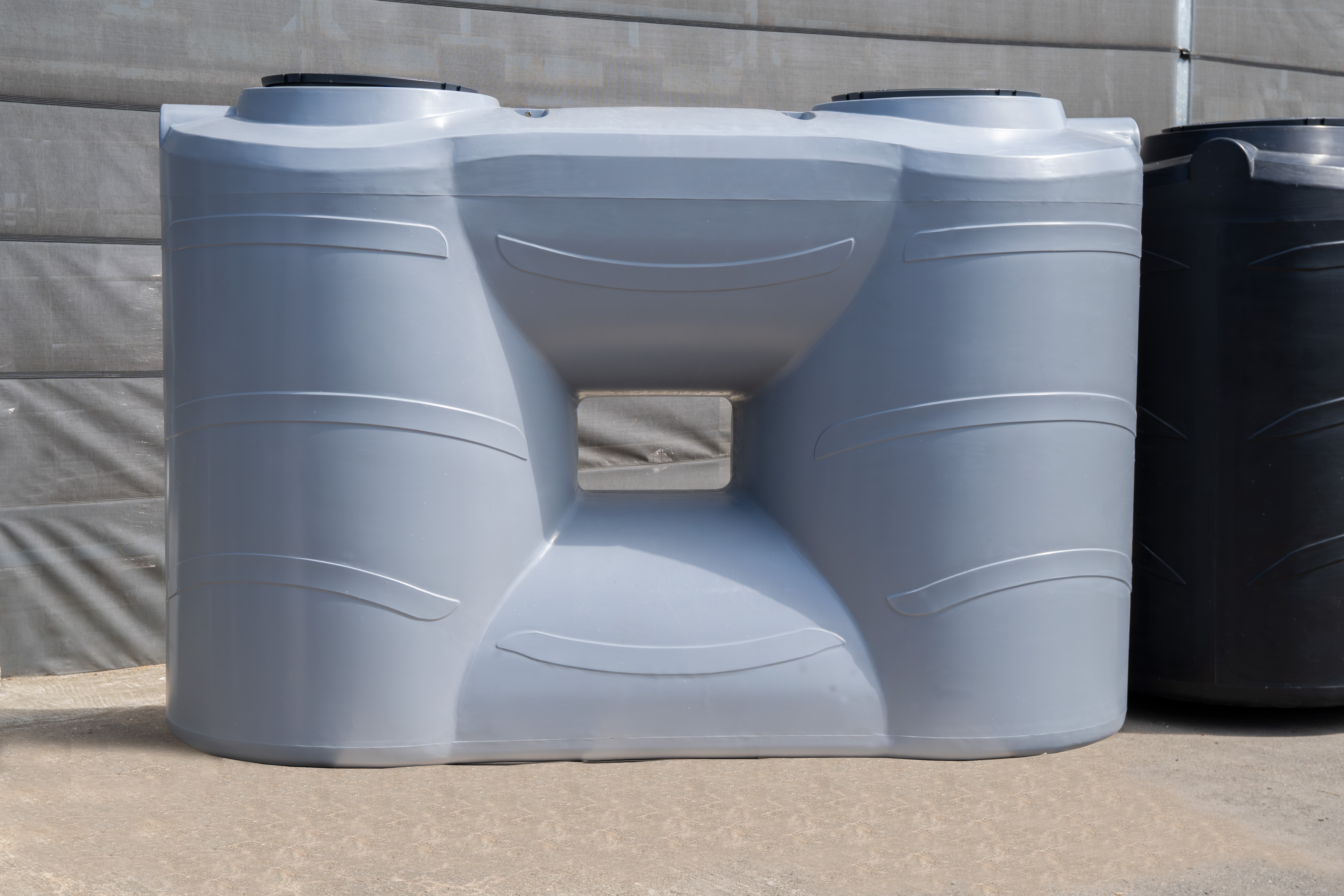 5000-Liter-Wassertank in Grau mit zwei Deckeln, vorne abgebildet, mit schwarzem Tank im Hintergrund für Regenwasserspeicherung